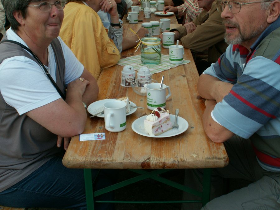 Zwei Personen sitzen mit Tassen und Kuchen an einem Holztisch im Café.